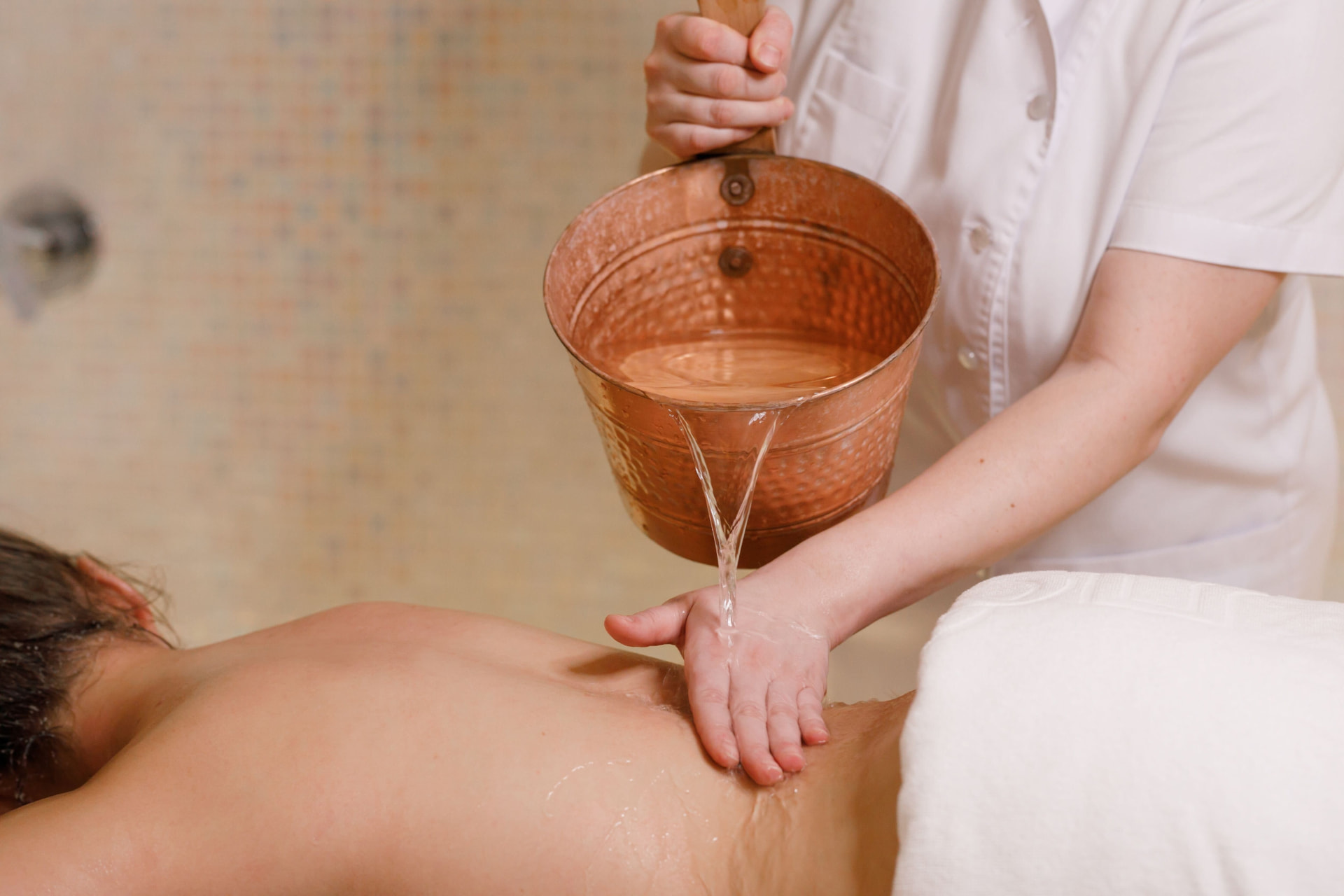Therapist rinsing a guest with a copper bowl of warm water